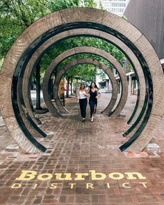 two women are walking down the sidewalk in front of an arch that reads bourbon district