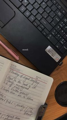 an open notebook sitting on top of a wooden desk next to a laptop and keyboard