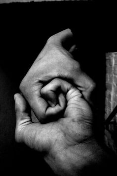 black and white photograph of two hands holding each other's fingers in front of a brick wall