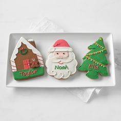 three decorated cookies in the shape of christmas trees and santa clause on a white plate