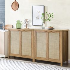 a wooden cabinet with three doors and two vases on the top, in front of a white wall