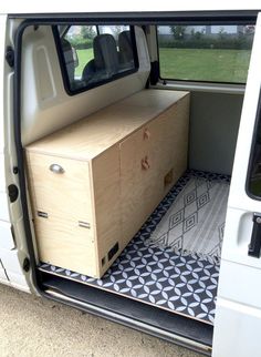 the interior of a van with an open door and drawers on the side, in front of a grassy field