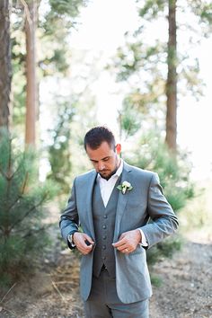 a man in a gray suit is looking down at his watch while standing on the ground