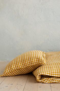 two yellow and white gingham pillows sitting on top of a wooden floor next to a wall