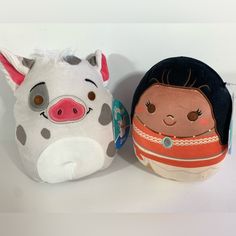 two stuffed animals sitting next to each other on a white surface with one pig and the other pig