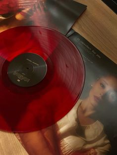 a red vinyl record sitting on top of a wooden table next to a cd case