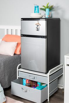 a silver refrigerator freezer sitting on top of a metal drawer next to a bed