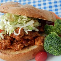 a pulled pork sandwich with coleslaw, tomatoes and broccoli on a white plate