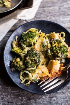 a black plate topped with broccoli covered in cheese and sauce next to a fork