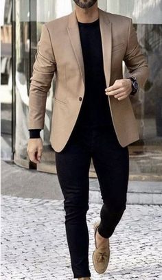 a man in a tan blazer and black shirt is walking down the street with his hand on his hip