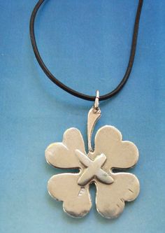 a silver pendant with four leaf clover on a black leather cord, sitting on a blue background