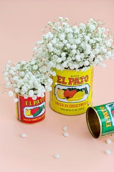 two tins filled with baby's breath flowers on top of a pink surface