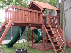 a wooden playset with a green slide and swing set in the back yard next to a tree