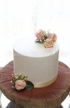 there is a white cake with flowers on the top and bottom, sitting on a wooden stand