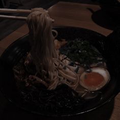 noodles and eggs in a black bowl with chopsticks