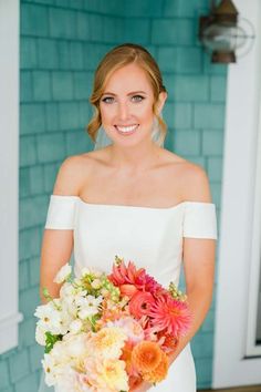 a woman holding a bouquet of flowers in front of a blue building with a brick wall