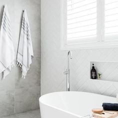 a white bath tub sitting under a window next to a sink and towel rack in a bathroom