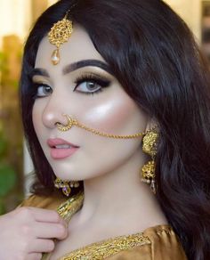 a woman with dark hair and gold jewelry on her face is posing for the camera