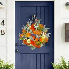 a blue front door with an orange wreath on it and two potted plants next to it