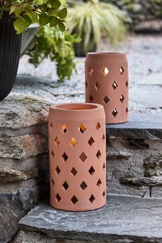 two vases sitting next to each other on a stone wall near a potted plant