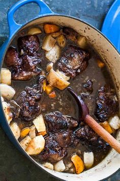 a pot filled with stew and potatoes on top of a table next to a wooden spoon