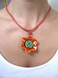 a woman wearing a necklace with an orange flower and a green button on the center