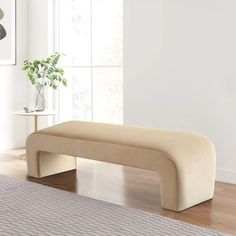 a beige bench sitting on top of a hard wood floor next to a white wall