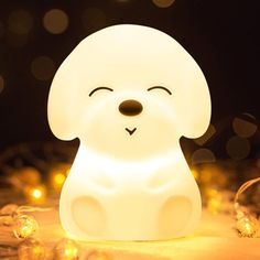 a white dog shaped night light sitting on top of a wooden table next to christmas lights