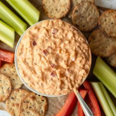 a bowl of dip surrounded by crackers, celery and carrots