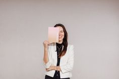 a woman is holding up a book in front of her face while standing against a wall