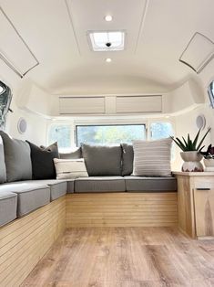 the inside of a camper with wood flooring and couches, windows, and potted plants