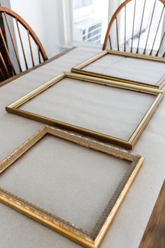 three frames sitting on top of a table with chairs in the background and one is empty