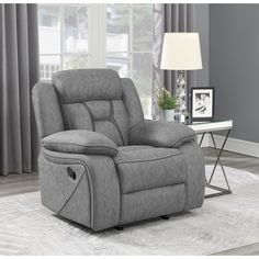 a gray recliner chair sitting on top of a rug in front of a window