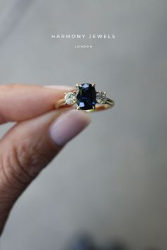 a woman's hand holding an engagement ring with two diamonds on the side and a blue sapphire in the middle