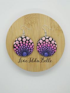 a pair of pink, purple and black earrings on a wooden plaque with the word love in it