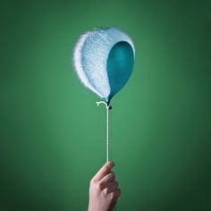 a hand holding a blue and white ballon with string attached to the end, on a green background