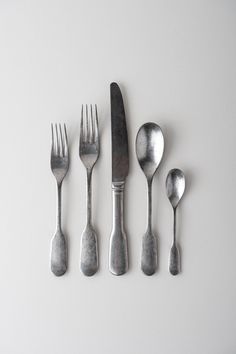 five spoons, two forks and one knife on a white surface