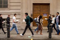 people walking on the sidewalk in front of a building with doors and windows, some carrying bags