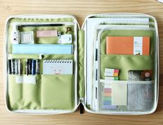 an open green case filled with lots of office supplies on top of a wooden table