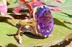 "The Brookside Outstanding Amethyst Cocktail Ring. The ring features an amazing, over 20 carat oval brilliant cut vivid purple amethyst in the center. Finished with a mid century modern filigree type shank in the through finger view the ring makes a statement. The ring is crafted in 18 karat yellow gold and is signed by the designer with the hallmark \"CB\" Yet we have not quite identified the craftsman quite yet. An amazing statement piece and a benchmark for the mid century modern era. Each pi Art Deco Purple Amethyst Ring For Formal Occasions, Purple Amethyst Art Deco Ring For Formal Occasions, Formal Art Deco Purple Amethyst Ring, Art Deco Oval Amethyst Ring, Modernist Oval Rings For Formal Events, Modernist Oval Rings For Formal Occasions, Art Deco Amethyst Oval Ring, Modern Amethyst Ring With Center Stone For Formal Occasions, Elegant Oval Purple Rings