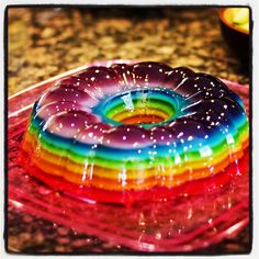 a rainbow donut sitting on top of a glass cake plate with sprinkles