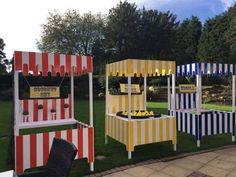 three carnival booths with signs on them sitting in the grass