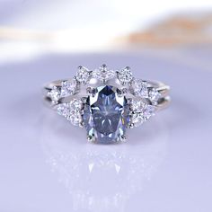 a fancy ring with an oval blue diamond surrounded by smaller round diamonds on a white surface