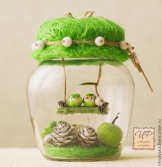 a glass jar filled with fake grass and pine cones