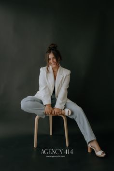 a woman sitting on top of a wooden chair in front of a black background and smiling