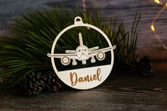 a personalized ornament with an airplane on it and pine cones in the background