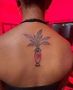 the back of a woman's shoulder with a vase and leaves tattoo on it