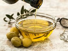 olives and oil are being poured into a bowl