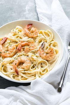 a white bowl filled with pasta and shrimp on top of a table next to silverware