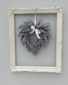 a heart shaped lavender wreath hangs in a frame on the wall next to a gray wall